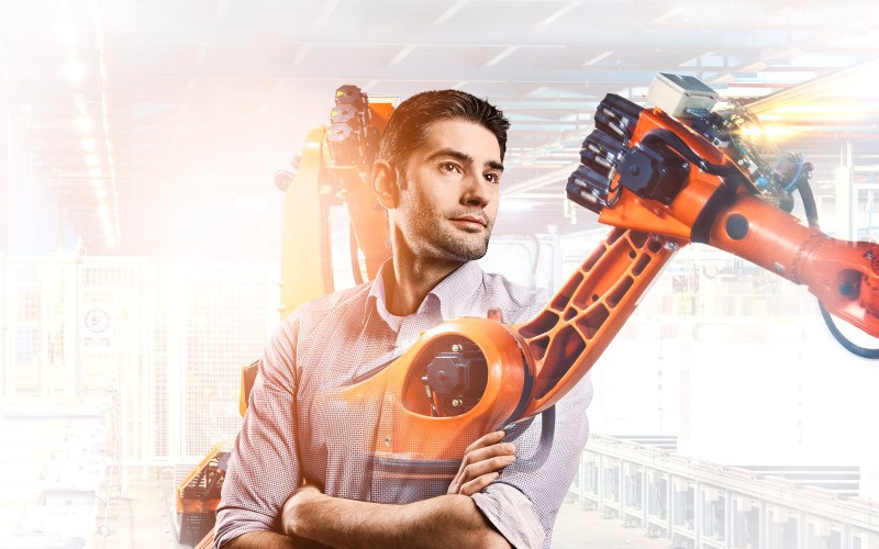 Konstrukteur Fabian mit Fertigungsroboter im Hintergrund