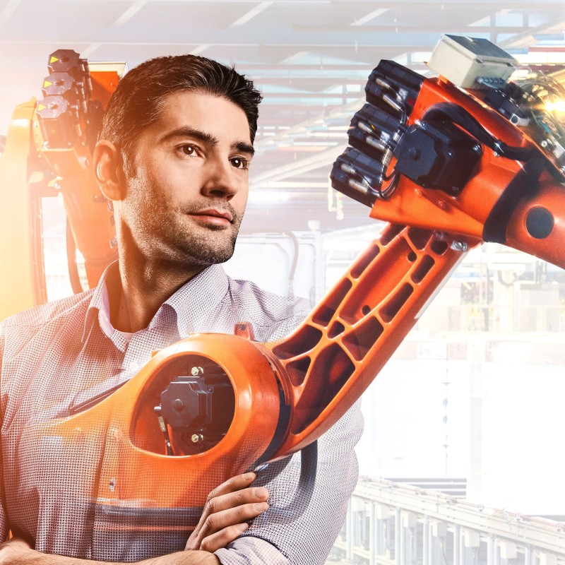 Konstrukteur Fabian mit Fertigungsroboter im Hintergrund