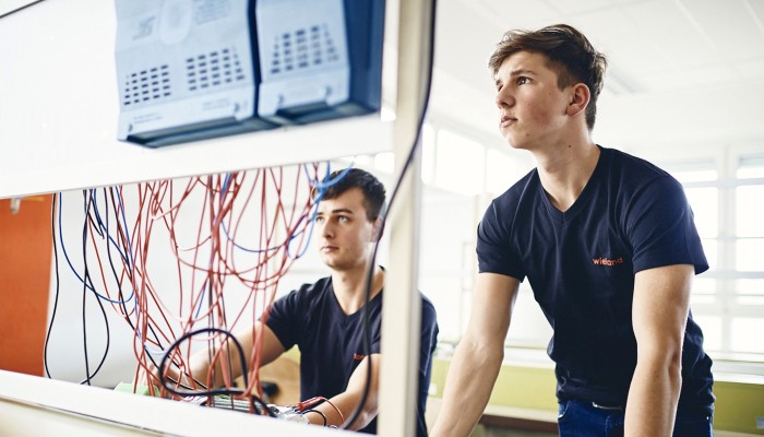 Auszubildender Noah mit Arbeitskollegen an Steuerpult