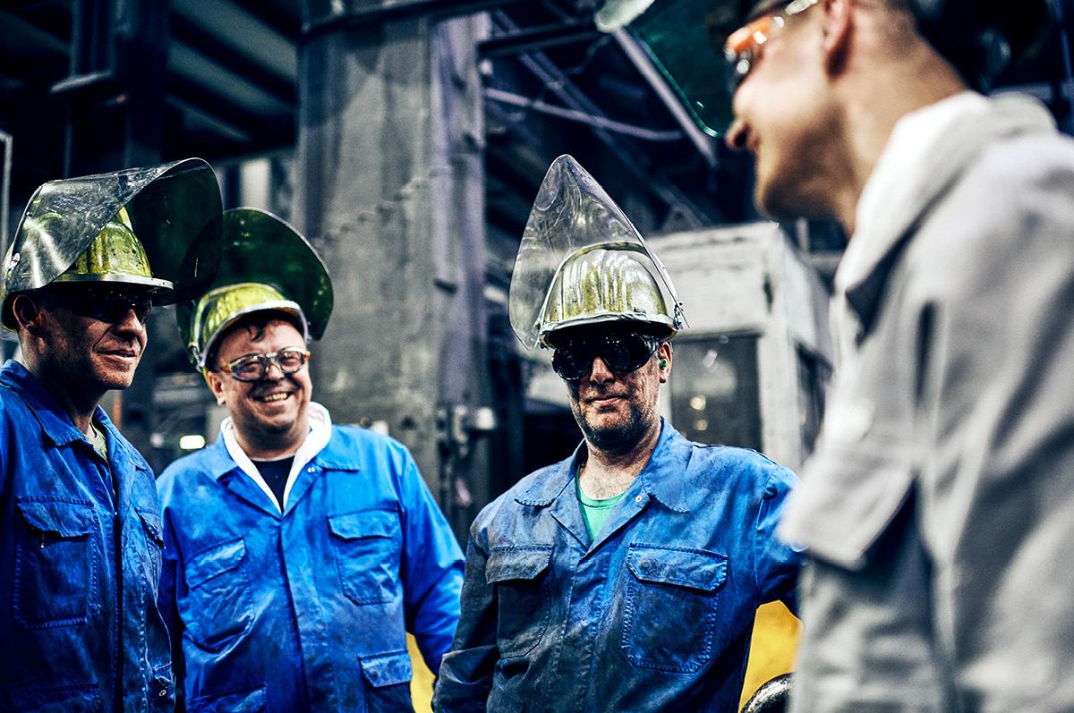 Gruppe von Mitarbeitern der Fertigung stehen in Schutzkleidung lachend zusammen