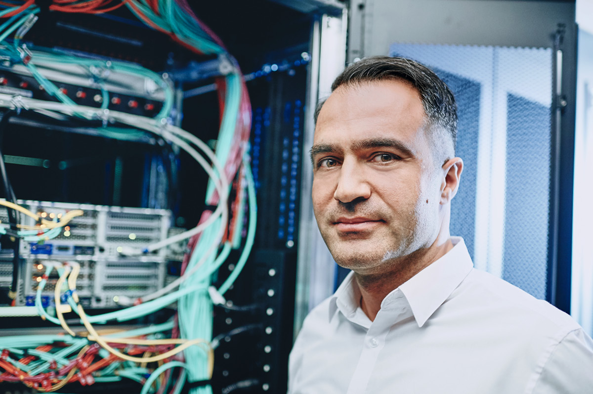 IT-Experte steht vor Serverschrank und blickt in die Kamera