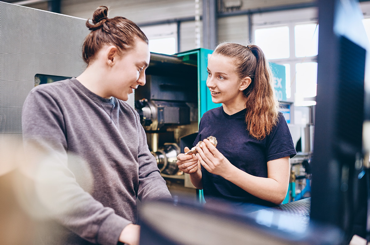Zwei weibliche Auszubildende sprechen über eine Kupfer-Komponente