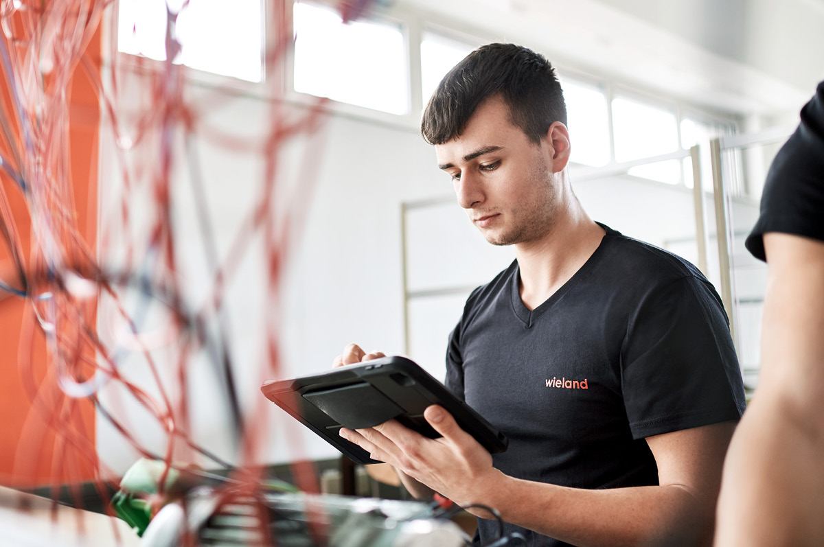 Junger Praktikant in Arbeitskleidung hält Tablet in der Hand
