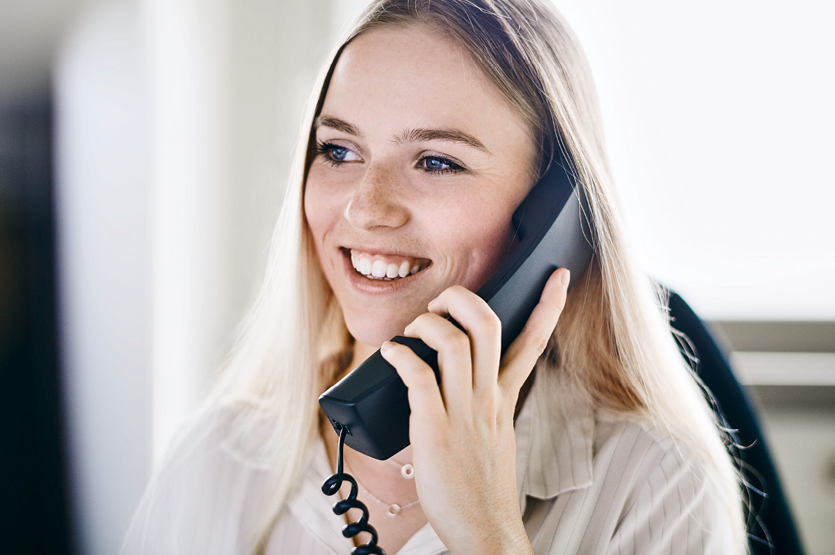 Junge, lächelnde Mitarbeiterin aus der Verwaltung ist am Telefon